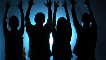 Four people offering praise or worship. Spirituality. Blue light background. Cult, religion, followers. Silhouette.