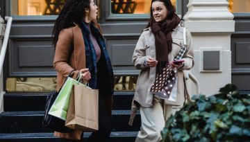 amazed young multiracial women gossiping while strolling on street with shopping bags
